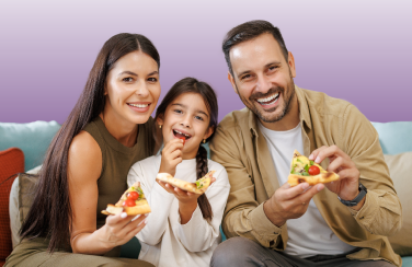 family of three sitting on a couch eating pizza