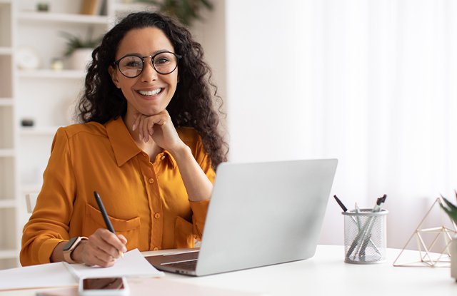 woman on her laptop smiling with a pen in her hand