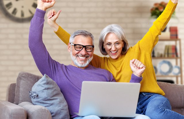 image of a couple sitting on a couch looking at a laptop while cheering