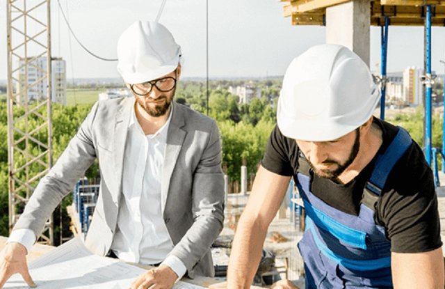 2 men with hard hats looking over building plans
